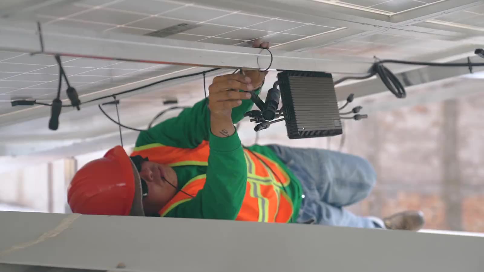 Solar-Monteur verkabelt und verzurrt Photovoltaik-Module unter dem Modultisch – echte Baustelle